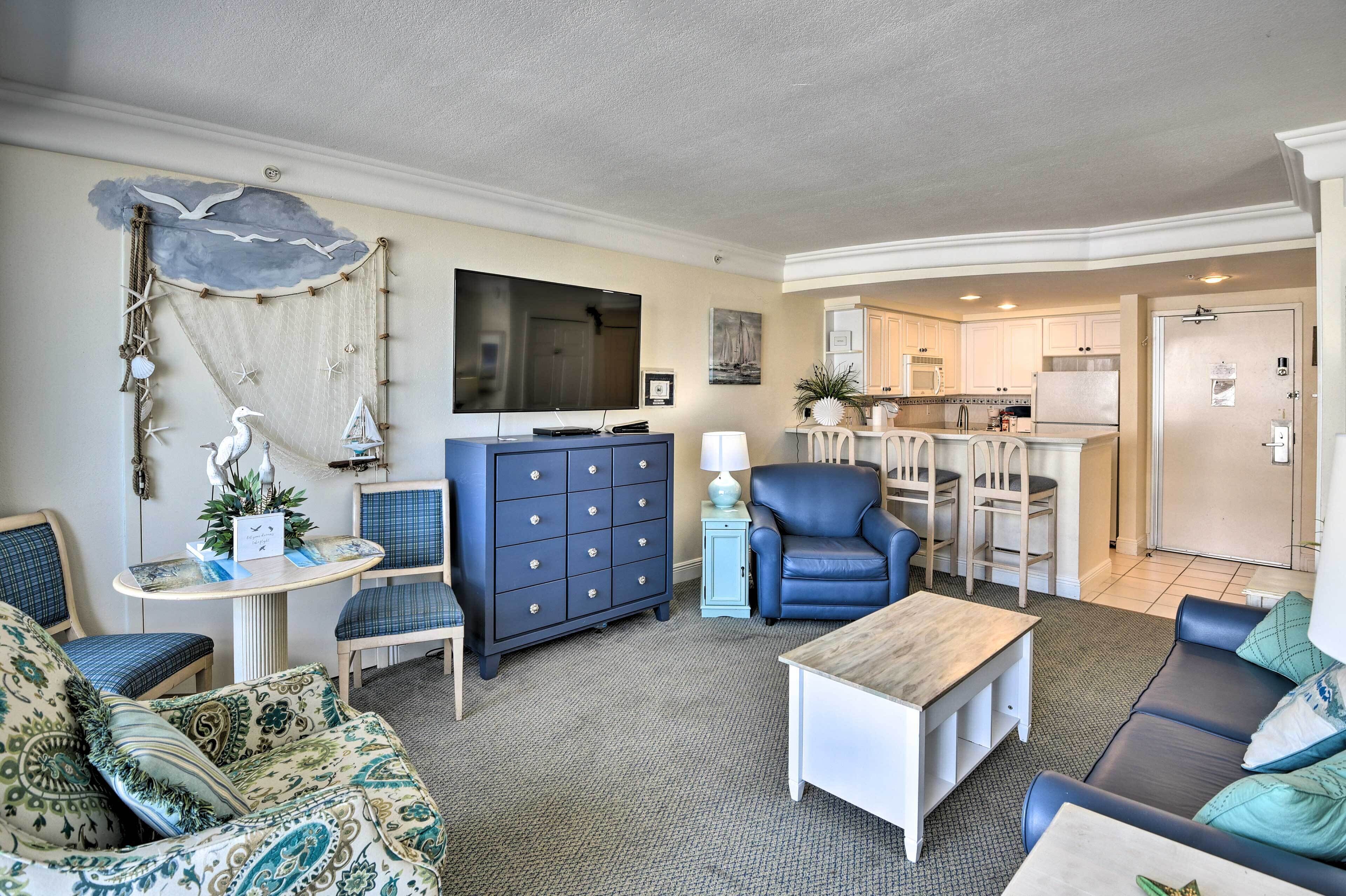 Una sala de estar con sofá, sillón, mesa de centro, un sillón azul, un mueble aparador y un televisor.