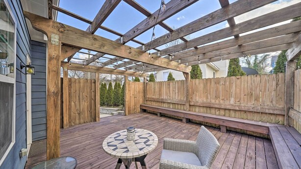 Eine Holzterrasse mit einem runden Tisch, Korbstühlen und einer Holzbank, sowie ein Pergolen-Überdachung.