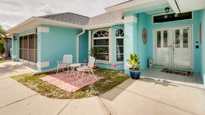 Une maison à la façade turquoise, un porche avec deux chaises blanches, un petit jardin et une plante en pot.