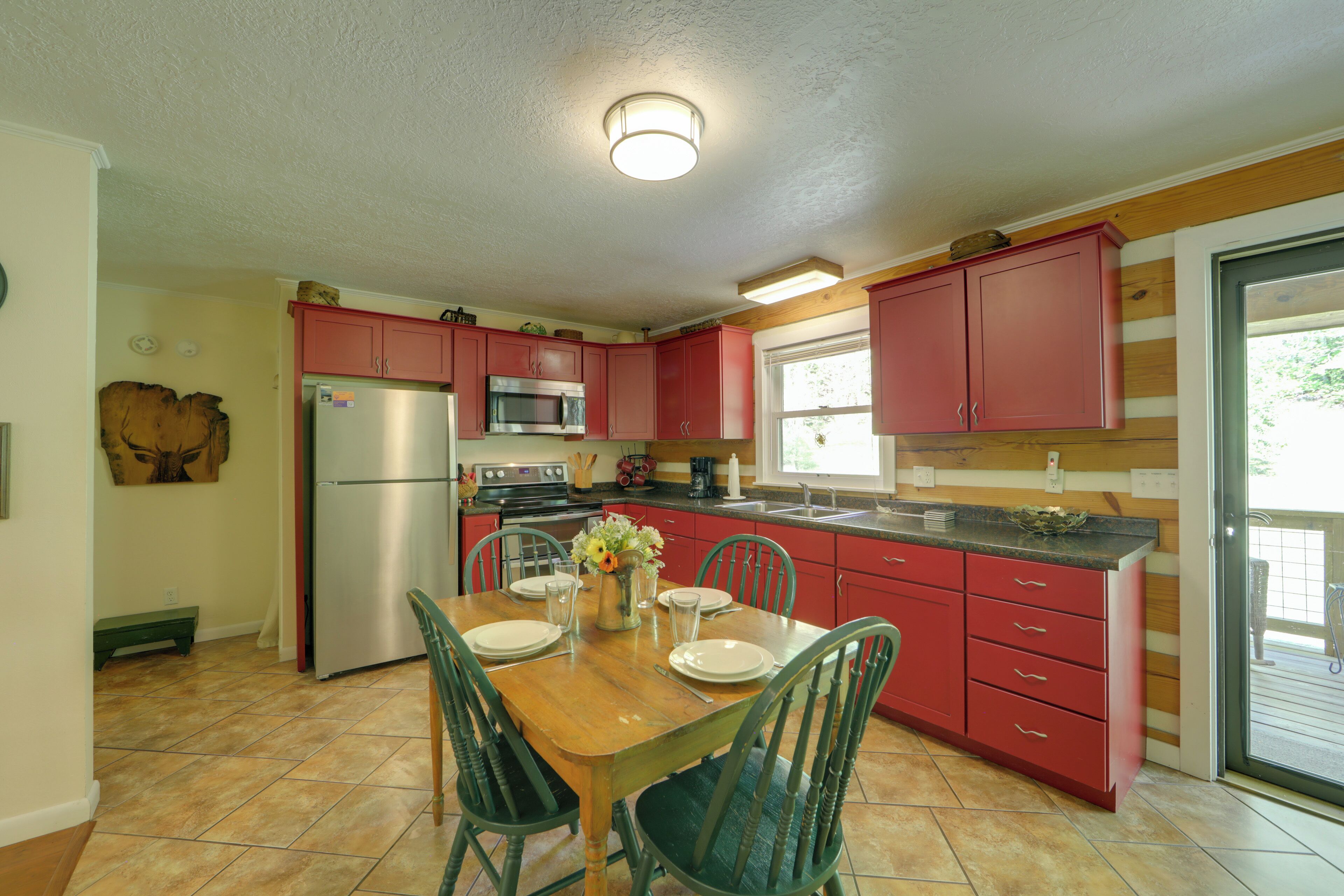 A kitchen with red cabinets, a stainless steel refrigerator, a microwave, and a sink. There is a dining table with chairs and a vase with flowers.
