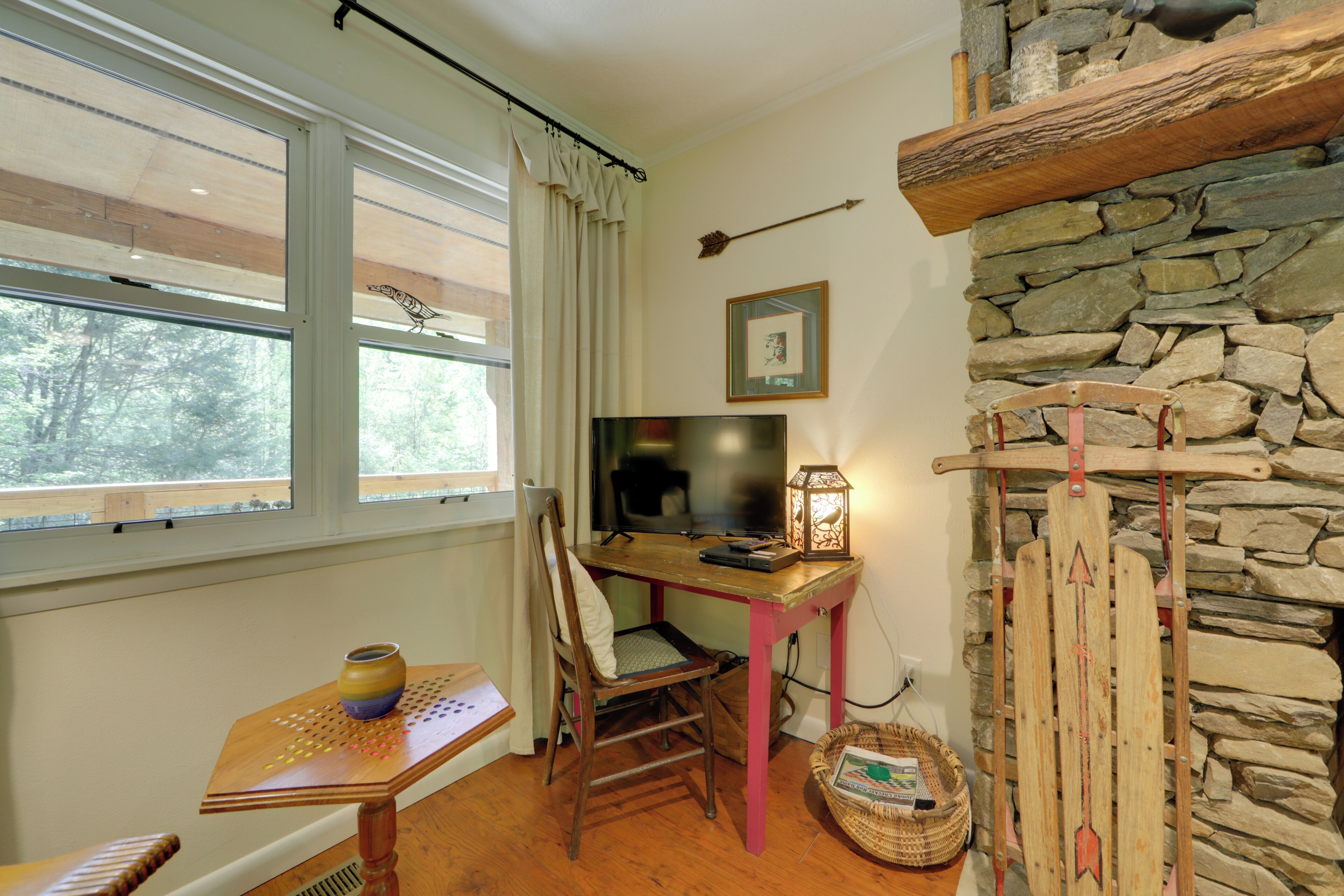 A cozy room with a wooden desk, a chair, a television, and a stone wall.