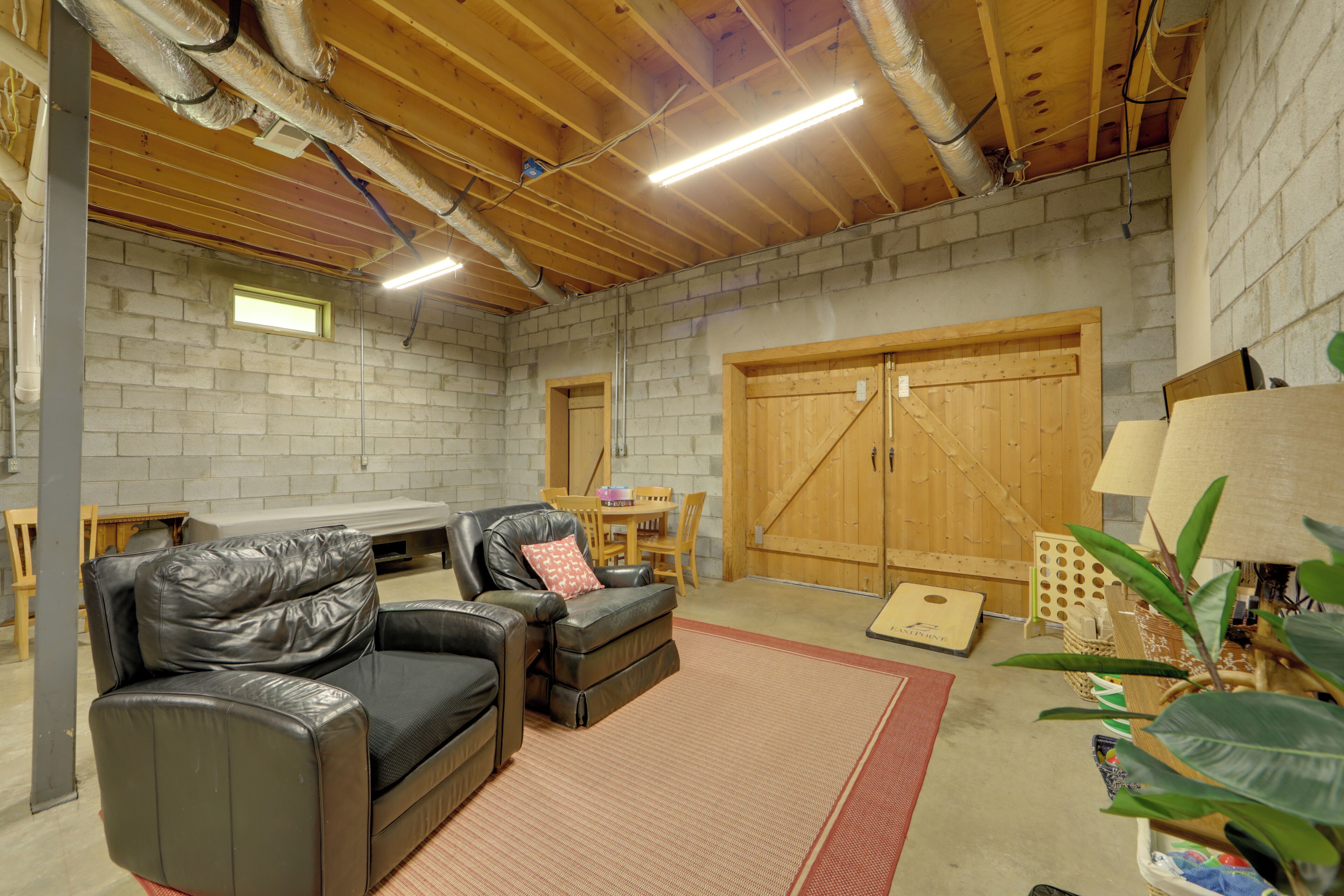 A basement with a wooden ceiling, brick walls, a leather sofa, a dining table, and a large wooden door.