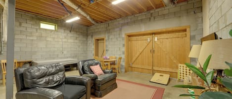 A basement with a wooden ceiling, brick walls, a leather sofa, a dining table, and a large wooden door.