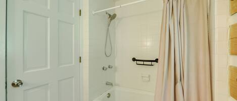 A bathroom with a white door, a bathtub, a showerhead, and a beige curtain.