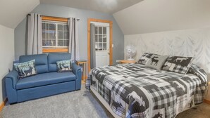 Une chambre à coucher avec un lit, un canapé bleu, une fenêtre avec des rideaux, une porte et un ventilateur mural.