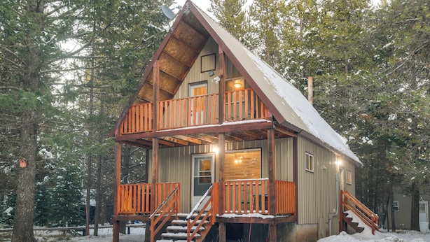 Une cabane dotée d’une terrasse en bois, d’un escalier et d’un toit recouvert de neige.