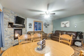A cozy living room with a stone fireplace, a television, a ceiling fan, and a large window. - Family Cabin - 25 Miles to Yellowstone Natl Park (Island Park)