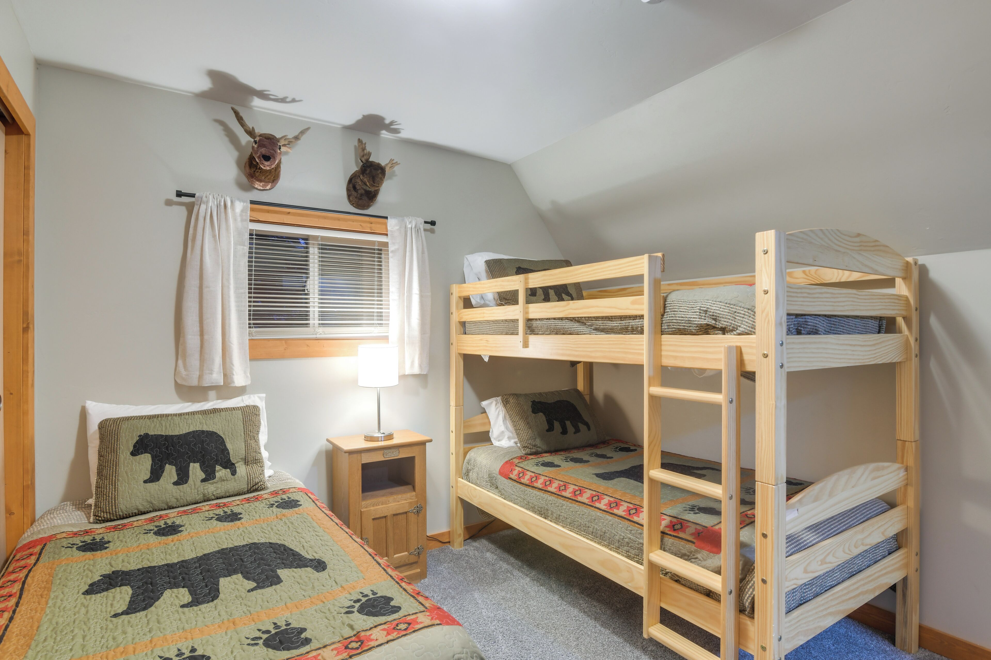 A room with two bunk beds, a small bedside table, a lamp, and a window with curtains.