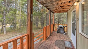 Une terrasse en bois avec un barbecue et une table, entourée d’arbres.