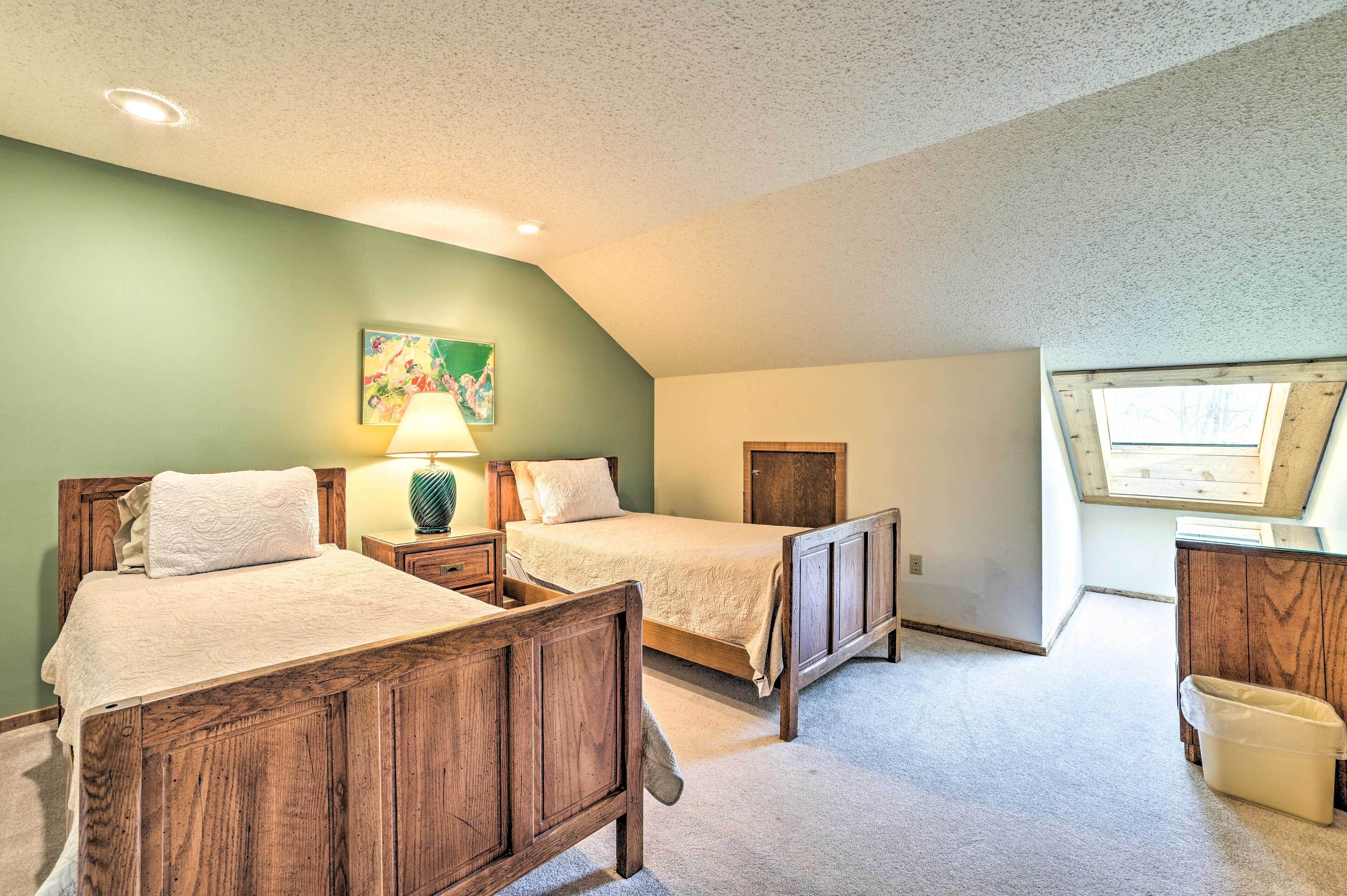 A bedroom with two wooden beds, a nightstand with a lamp, a wooden cabinet, and a skylight.