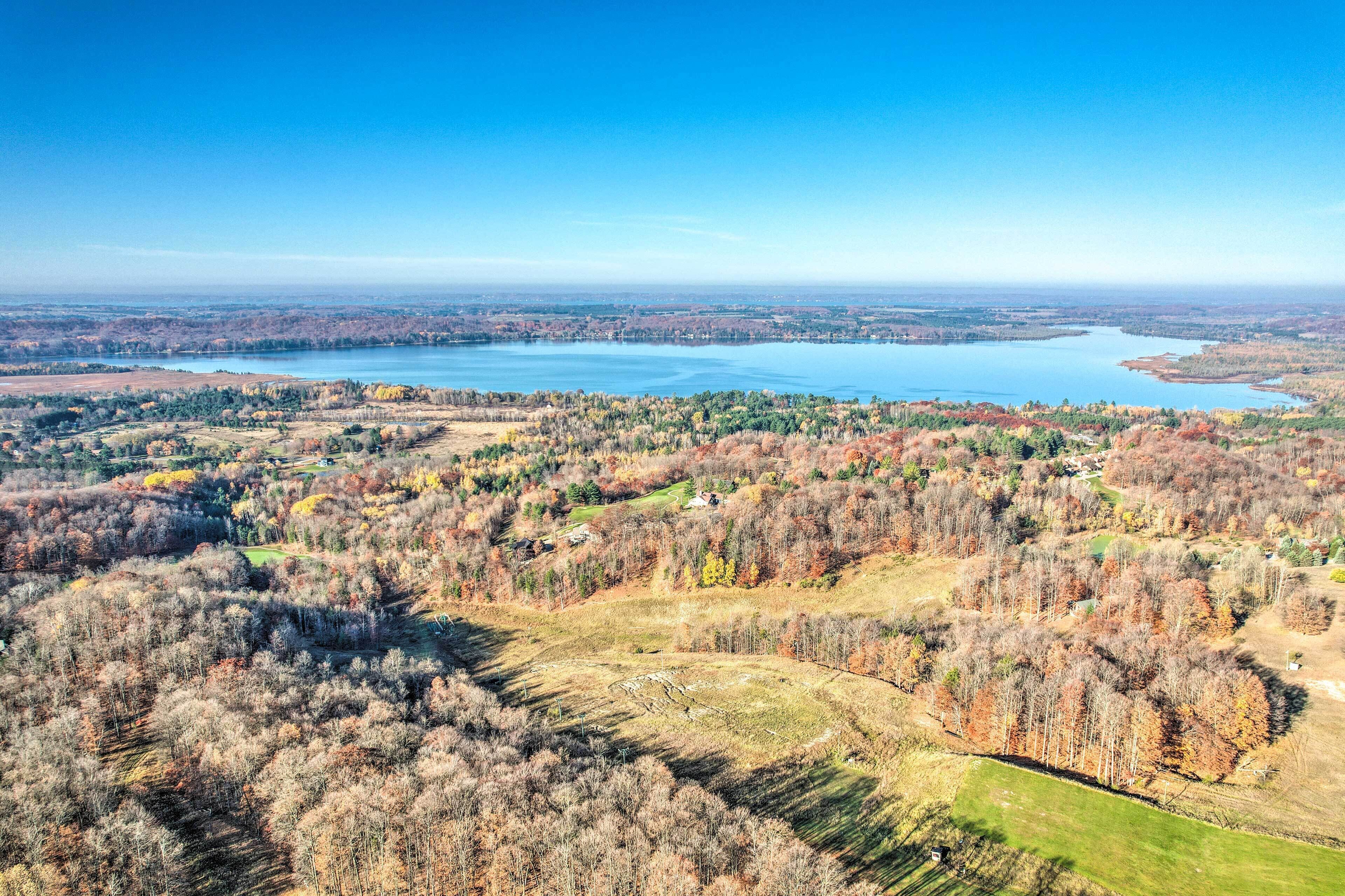 Vista panorâmica de uma paisagem à beira de um lago, com áreas arborizadas e céu azul límpido.