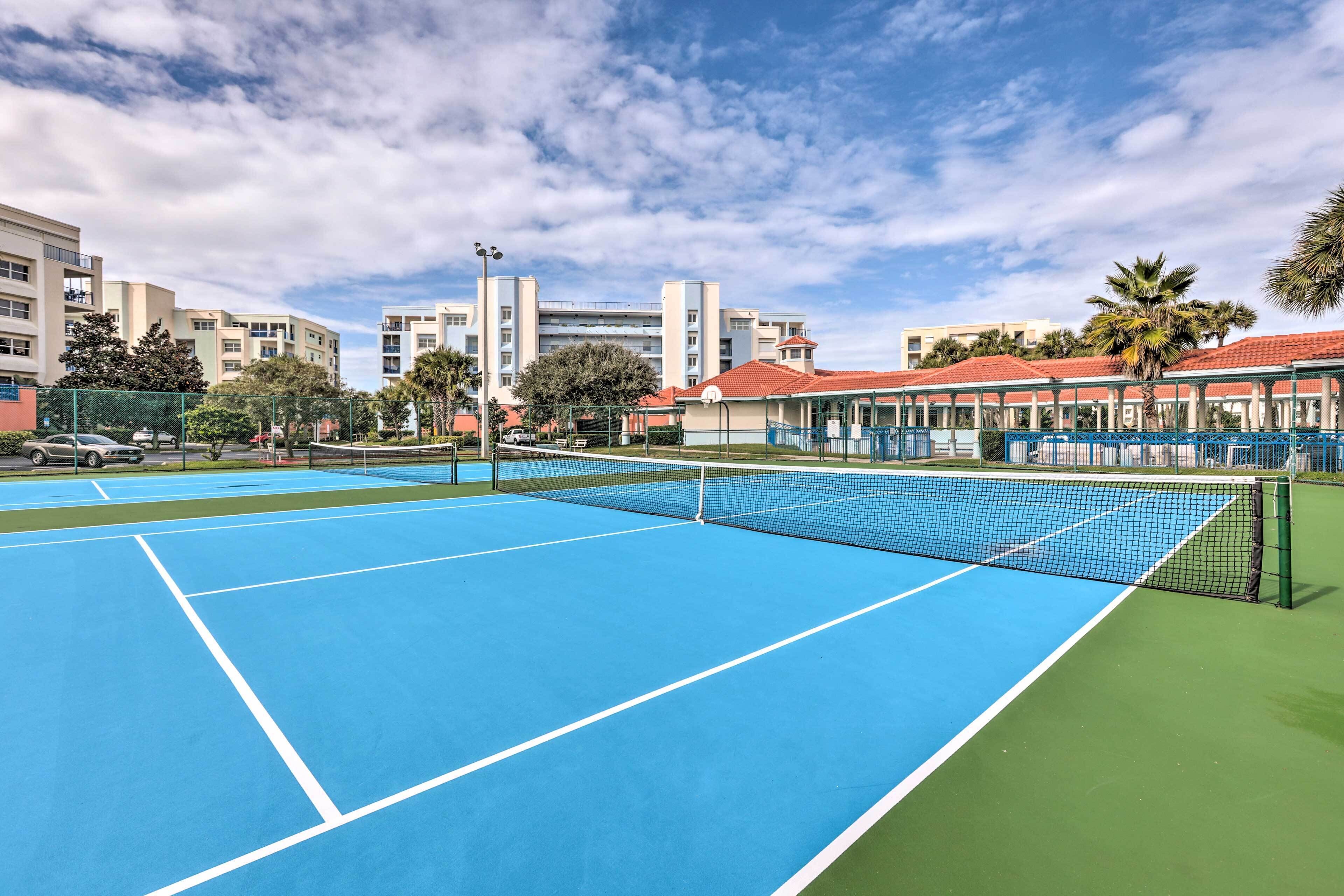 Una cancha de tenis con red, rodeada de edificios y palmeras.