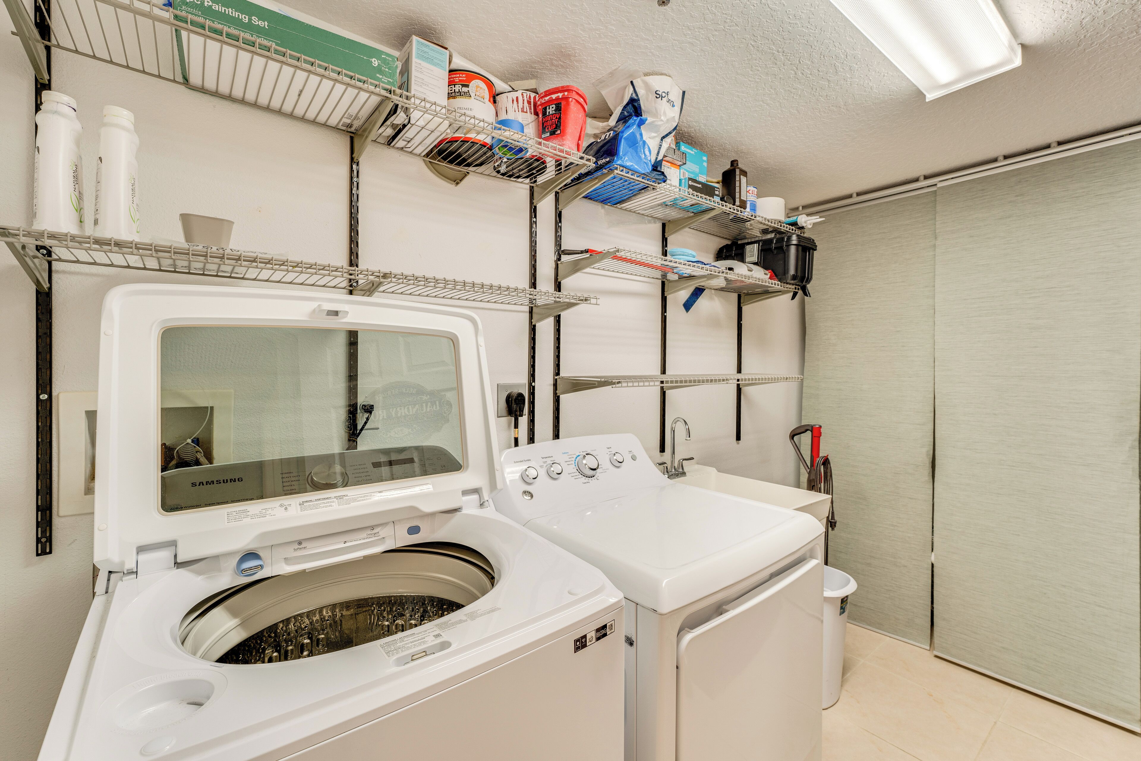A laundry room with a Samsung washer and dryer, shelves with cleaning supplies, and a closed closet door.