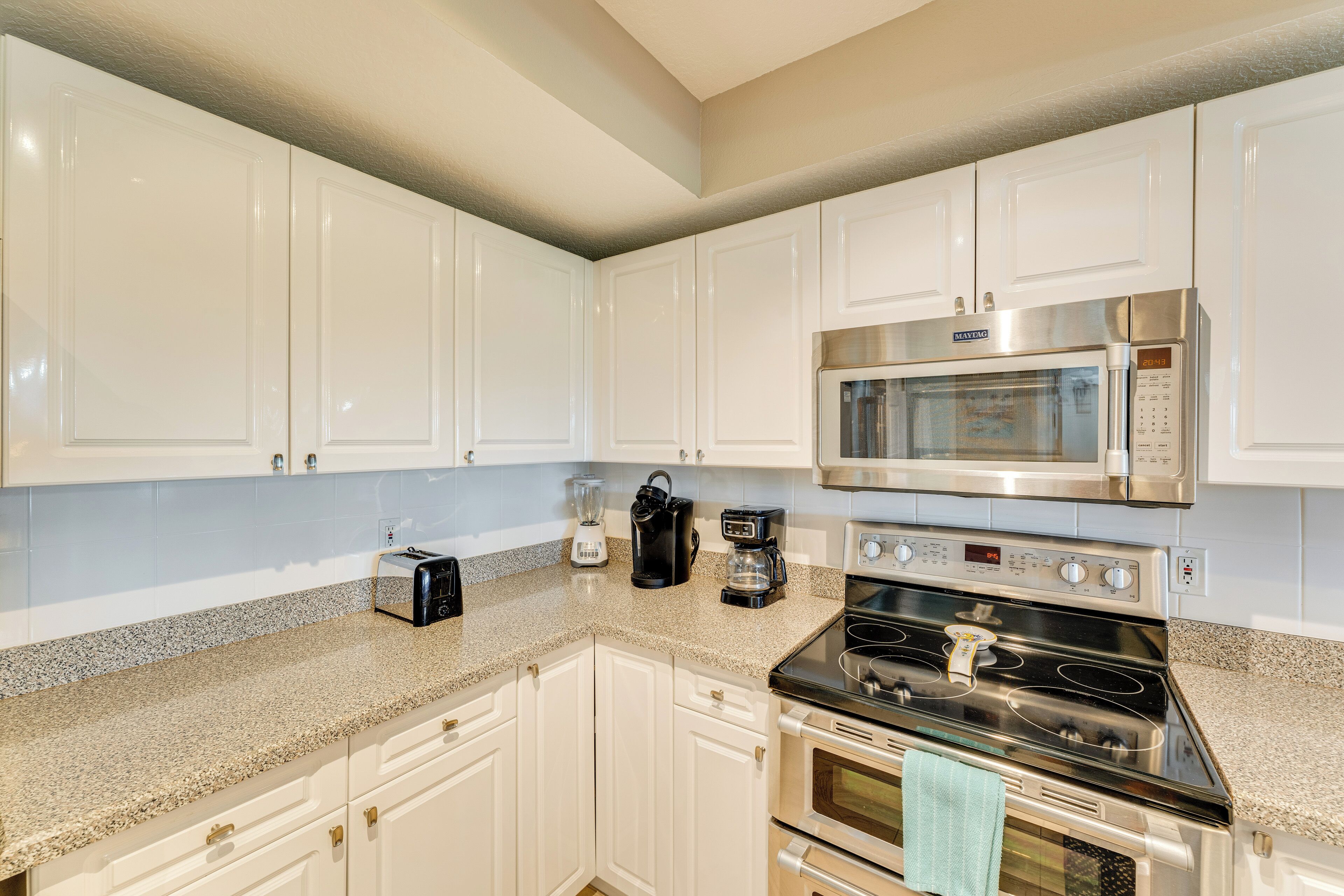 A kitchen with white cabinets, a stainless steel microwave, a stove, and a coffee maker.