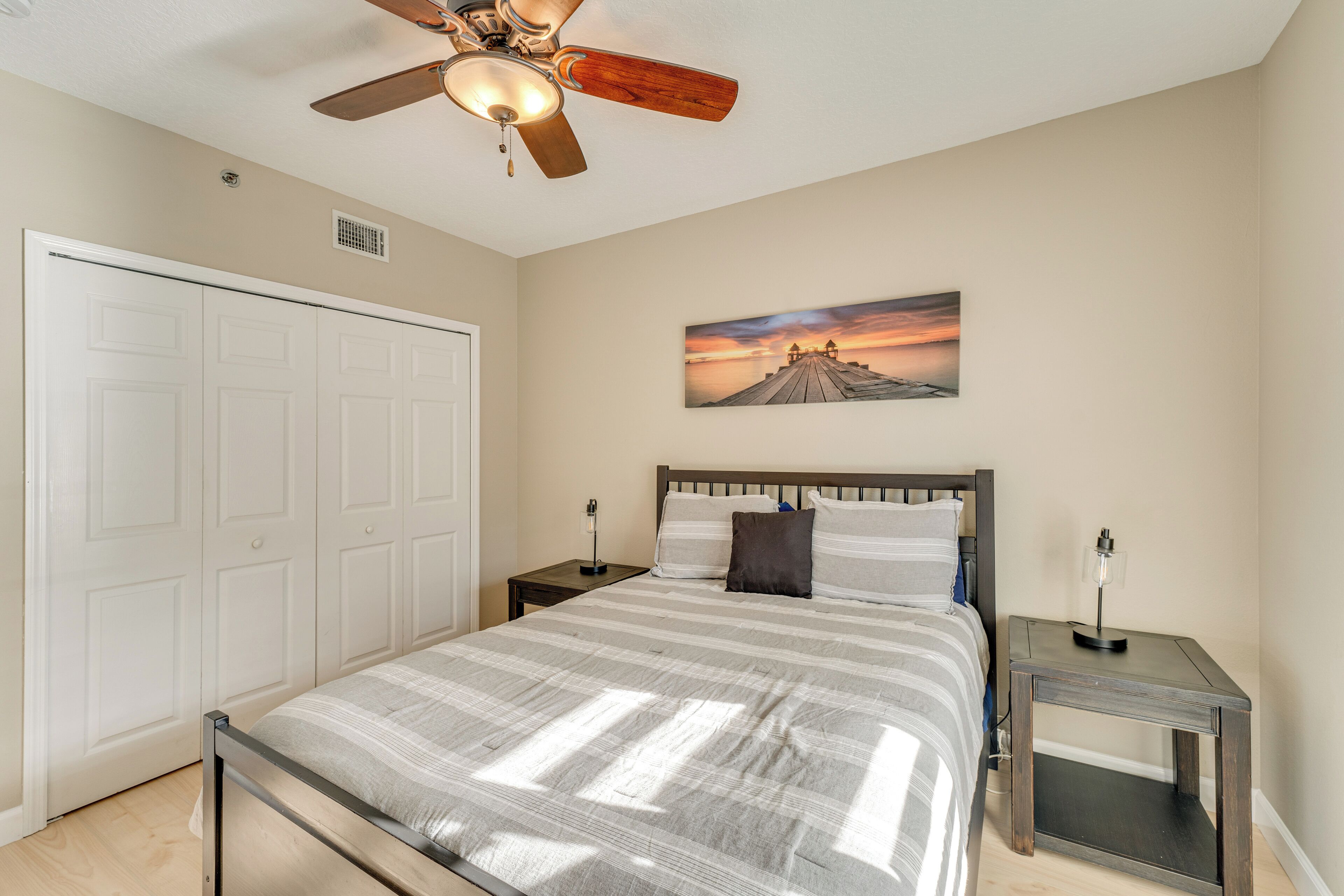 A bedroom with a bed, a ceiling fan, a nightstand, a wall-mounted lamp, and a door.