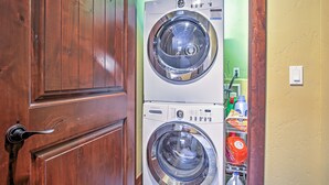 A laundry room with two stacked front-loading washing machines and a wooden door. - Lavish Fraser Townhome With Deck & Mountain Views! (Winter Park)