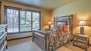 A bedroom with a large window, a wooden bed, two bedside tables with lamps, and a dresser. - Lavish Fraser Townhome With Deck & Mountain Views! (Winter Park)