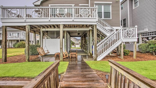 A wooden deck with a staircase leading to a covered area with outdoor furniture. - Spacious Beach Cottage w/ Private Dock Access (Ocean Isle Beach)