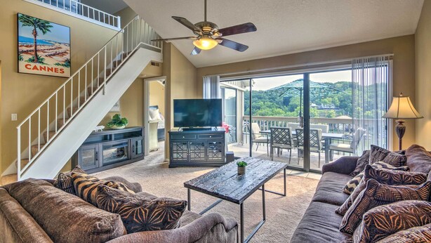 A spacious living room with a large TV, a ceiling fan, and a balcony with a scenic view.