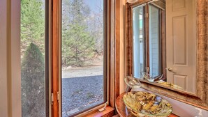 Une salle de bain dotée d’un grand miroir, d’un lavabo en verre et offrant une vue sur les arbres à l’extérieur.