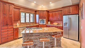Una cocina con armarios de madera, una isla central con taburetes, un refrigerador de acero inoxidable y un horno empotrado.