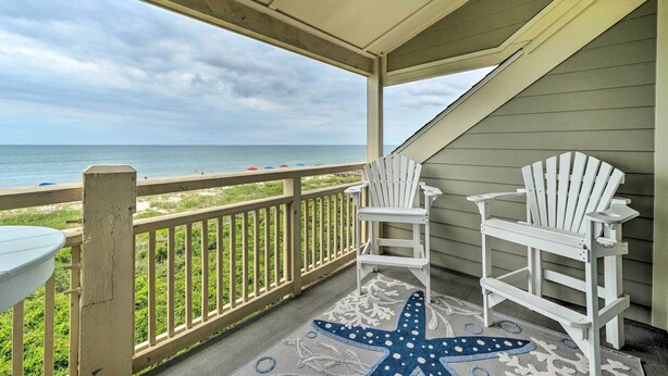 A covered balcony with two white Adirondack chairs, a white table, and a starfish-patterned rug. - Beachfront Condo w/ Unobstructed Ocean Views! (Oak Island)