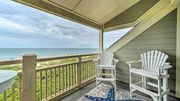 A covered balcony with two white Adirondack chairs, a white table, and a starfish-patterned rug.