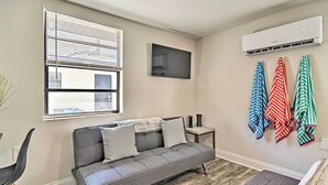 A modern living room with a grey sofa, a small side table, a mounted TV, and a window with blinds. - Pet-friendly Madeira Beach Studio Near Coast! (Madeira Beach)