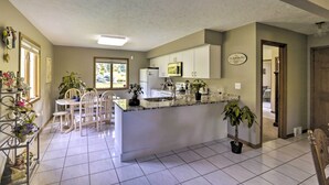 A kitchen with white cabinets, a granite countertop, and a central island. There are chairs around a dining table, and potted plants are placed around the room. - Charming Lewiston Apt: 10 Miles to Niagara Falls! (Lewiston)