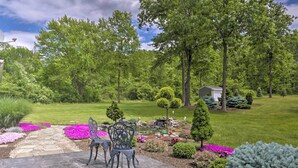 A patio with stone flooring and metal chairs, surrounded by a garden with various plants and flowers. - Charming Lewiston Apt: 10 Miles to Niagara Falls! (Lewiston)