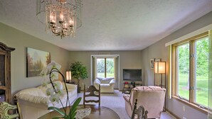A spacious living room with a large window, a chandelier, and a television. - Charming Lewiston Apt: 10 Miles to Niagara Falls! (Lewiston)