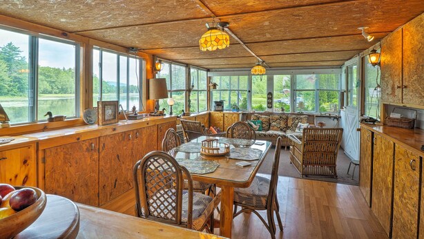 A spacious dining area with wooden tables and chairs, large windows offering views of the outdoors, and a wooden ceiling. - Cozy Cottage on Caroga Lake w/ Waterfront Fire Pit (Caroga Lake)
