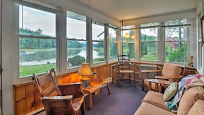 A cozy room with large windows overlooking a lake, wooden furniture, and a lamp. - Cozy Cottage on Caroga Lake w/ Waterfront Fire Pit (Caroga Lake)