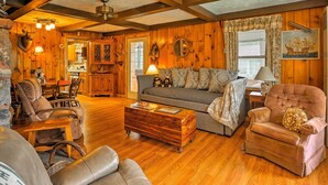 A cozy cabin interior with wooden walls, a dining area, and a living room furnished with leather sofas and a wooden coffee table. - Cozy Cottage on Caroga Lake w/ Waterfront Fire Pit (Caroga Lake)