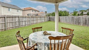A covered patio with a round table and four chairs, surrounded by a wooden fence and a grassy lawn. - Spacious Family Home Near San Antonio Hotspots! (San Antonio)
