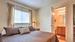 A bedroom with a large bed, a nightstand, a lamp, a window with curtains, and a view into the bathroom. - Spacious Family Home Near San Antonio Hotspots! (San Antonio)