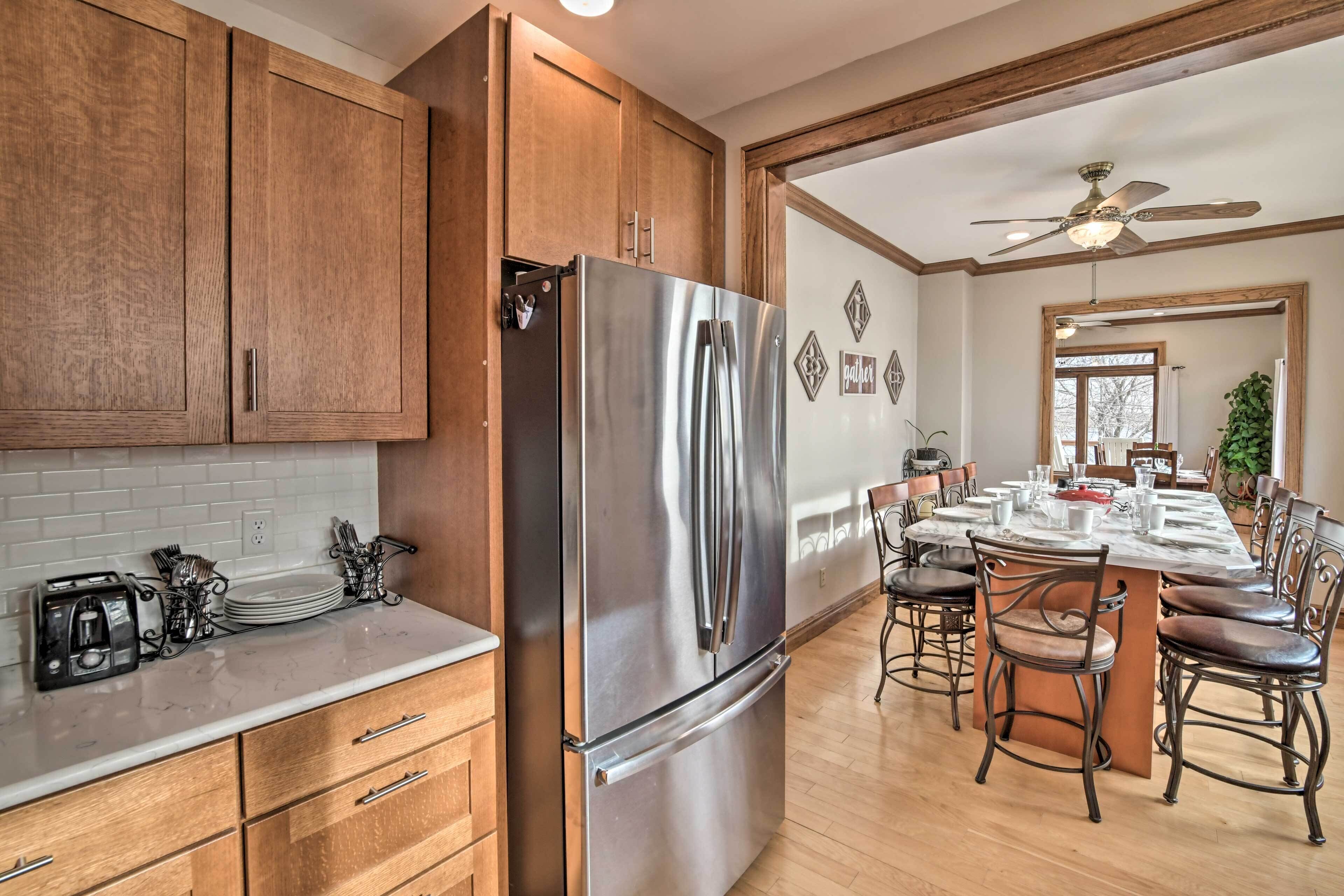 A kitchen with wooden cabinets, a stainless steel refrigerator, a marble countertop, and a dining area with a table and chairs.