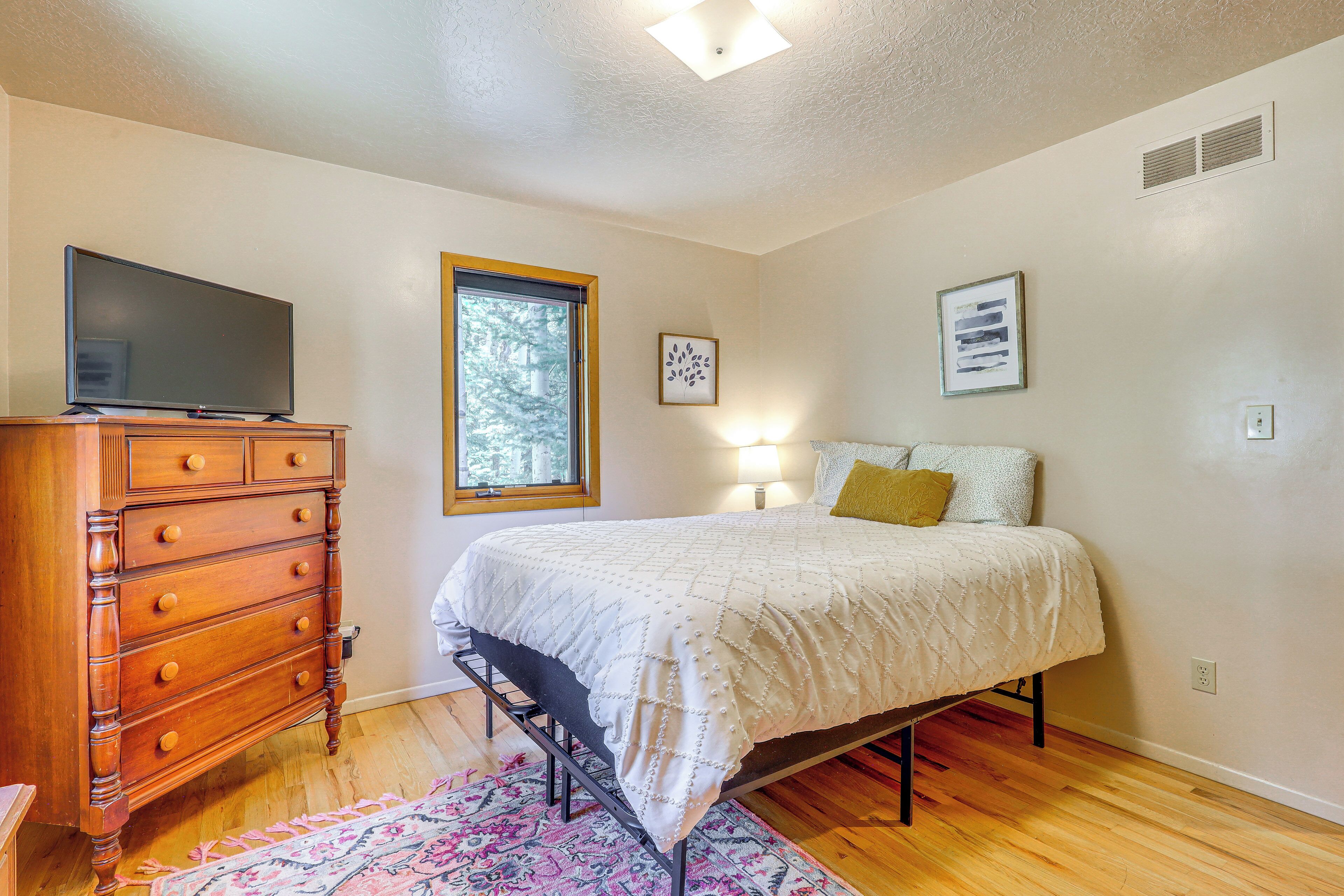 A bedroom with a bed, dresser, window, and artwork on the wall.