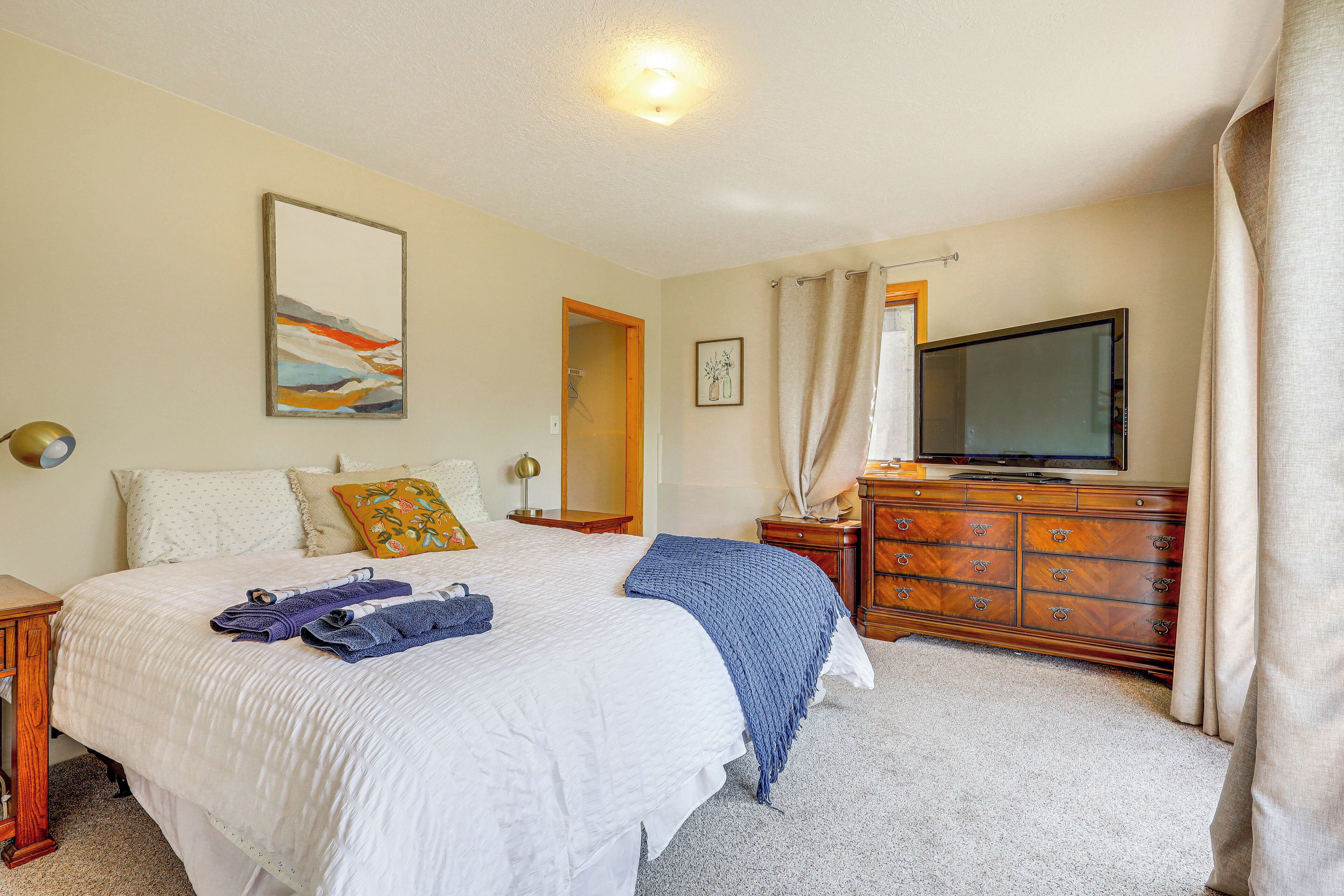 A hotel room with a bed, a dresser, a television, and a painting on the wall.