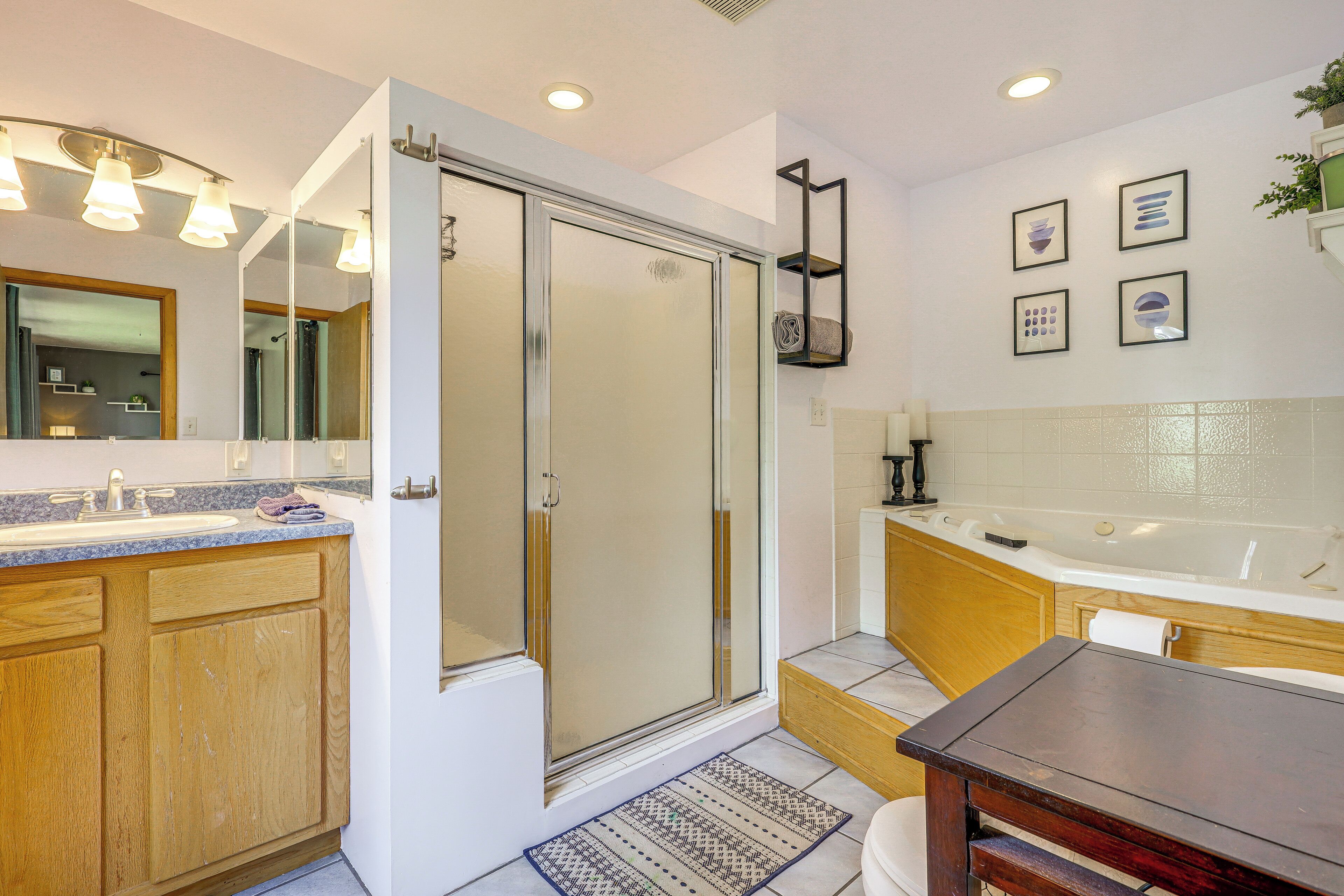 A modern bathroom with a glass shower enclosure, a wooden vanity, a bathtub, and a large mirror.