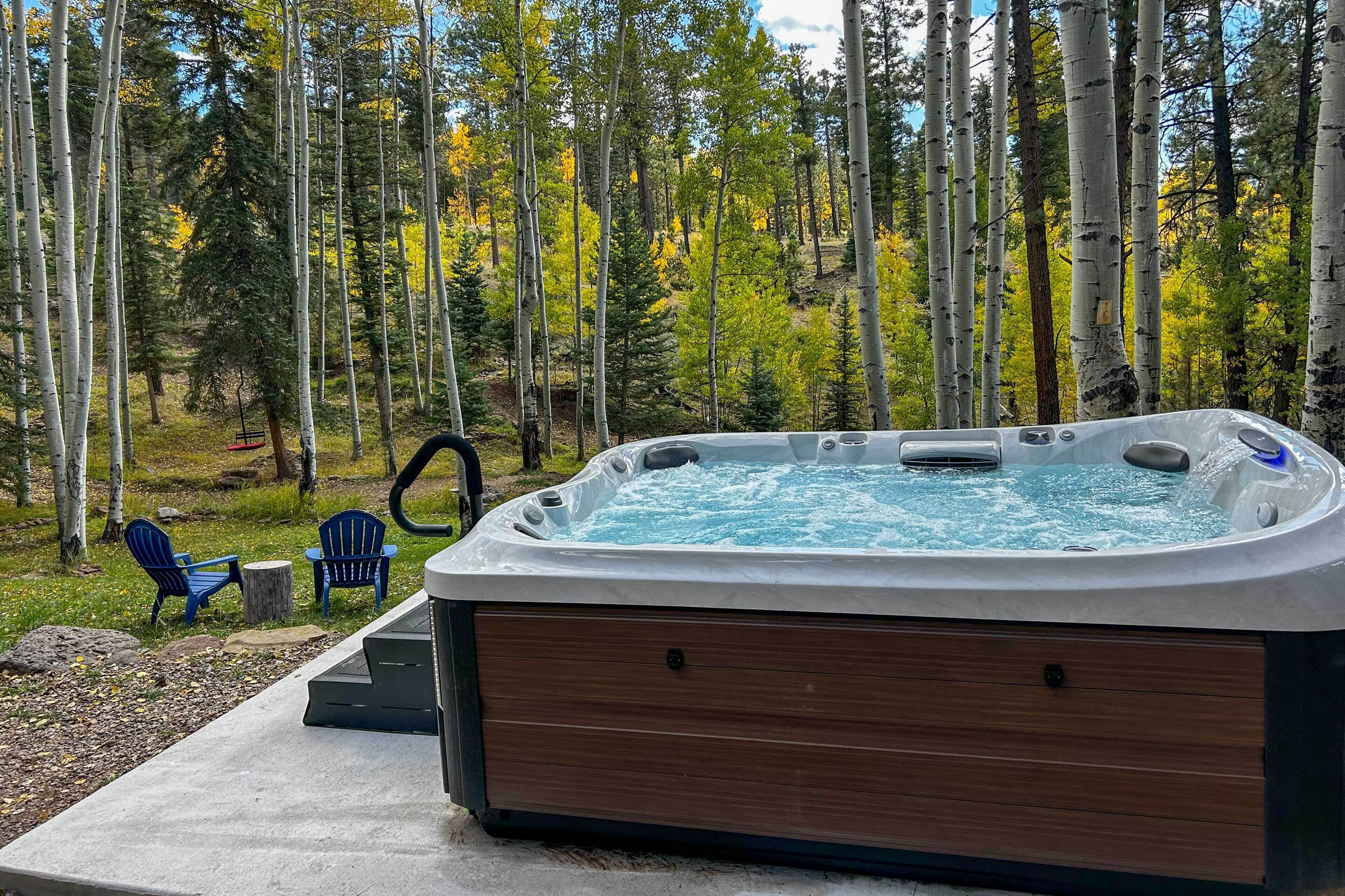 Een hottub in een bebost gebied, met twee blauwe stoelen en een kleine tafel.