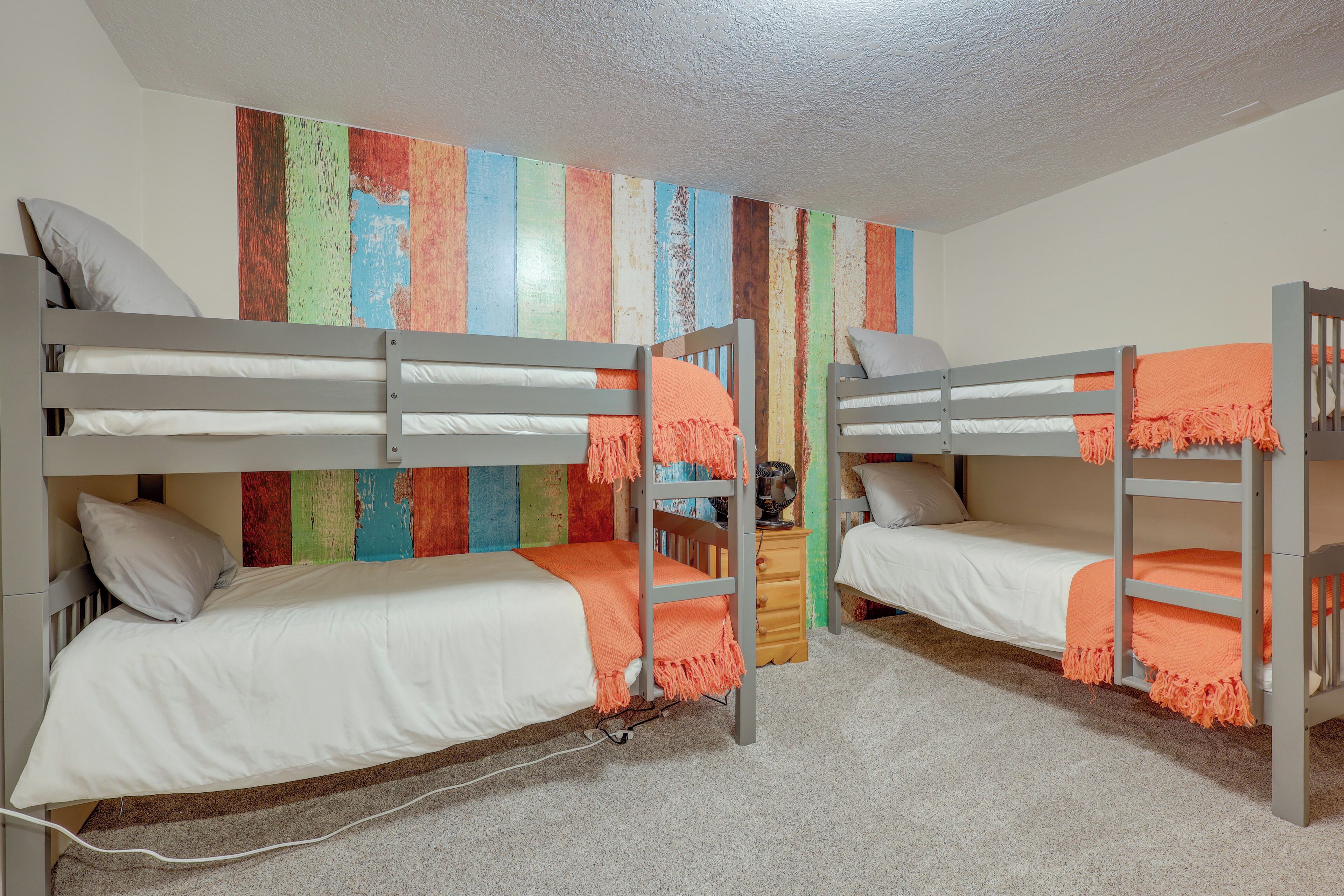 A bunk bed room with a colorful wall art, a wooden nightstand, and a carpeted floor.