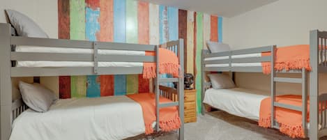A bunk bed room with a colorful wall art, a wooden nightstand, and a carpeted floor.