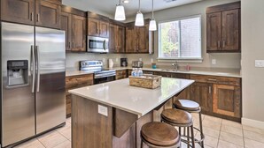 A modern kitchen with wooden cabinets, stainless steel appliances, a central island with stools, and pendant lighting. - Luxury Downtown Moab Townhome w/ Pool Access! (Moab)