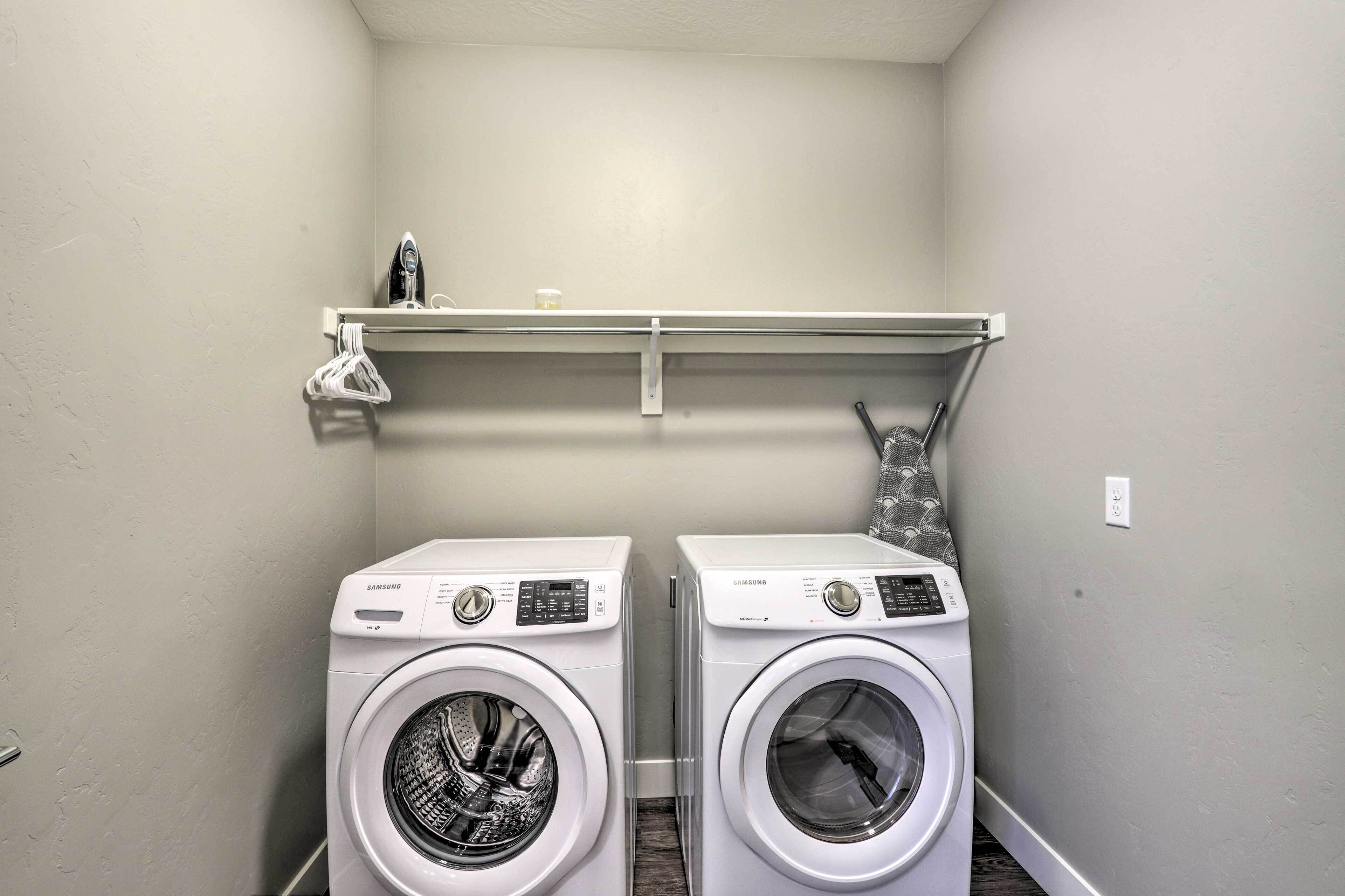 A laundry room with two white Samsung washing machines, a shelf above holding a few items, and a wall socket.