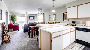 A modern kitchen with a central island, wooden cabinets, and a dishwasher. There is a dining area with a red sofa and a coffee table. - Beautiful Branson Condo w/ Golf + Pool Access! (Branson)