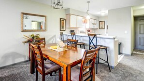 A dining area with a wooden table and chairs, a kitchen in the background, and a mirror on the wall. - Beautiful Branson Condo w/ Golf + Pool Access! (Branson)