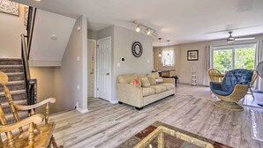 Amplia sala de estar con escaleras, un sofá color beige, un sillón de mimbre y una mesa de comedor con sillas.