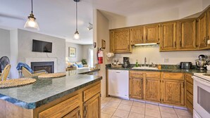 A kitchen with wooden cabinets, a dishwasher, a stove, and a dining area with chairs and a table. - Brigantine Retreat w/ Balconies - Walk to Beach! (Brigantine)