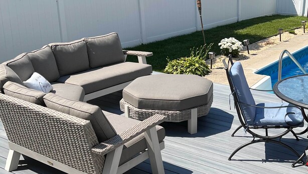 Een terras met een bank, voetenbankje en stoelen, een bijzettafeltje en een zwembad.